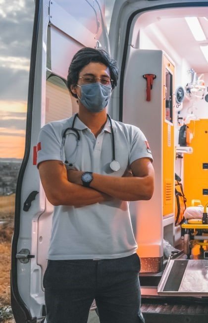 Portrait team of first aider healthcare emergency staff young doctor, paramedic worker man and young nurse woman dressed uniform and protective facemask  before the decontamination process for EMT, standing, arms crossed, smiling, looking at the camera posing in front of ambulance car at night during the covid19 pandemic after coronavirus quarantine and lockdown